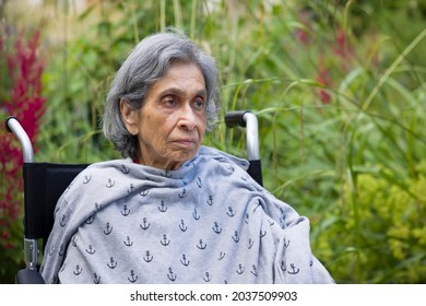Old woman, British Asian Indian, sitting in a wheelchair looking sad and worried. UK mental health concept, depression, healthcare and caring for the elderly
