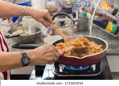 Old Woman Cooking Macaroni Pasta In Flying Pan In The Kitchen.