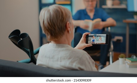 Old Woman With Crutches Using Video Call On Mobile Phone. Senior Adult Talking To Medic And Child On Online Teleconference To Start Remote Conversation. Grandmother With Smartphone.