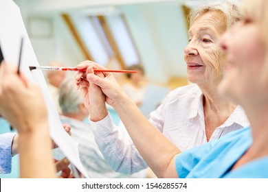 Old woman with dementia and therapist while painting in creative painting class