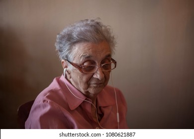 Old Woman With Earphones Listening To The Music.