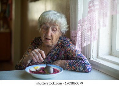 An Old Woman Eating Soup Sitting At A Table In The Her House.