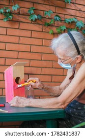 Old Woman With Face Mask Painting A Birdhouse