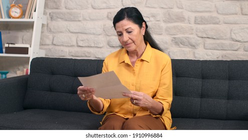 The Old Woman With Glasses Is Sitting On The Sofa, Reading The Letter. The Woman Is Upset And Crying Because Of The News In The Letter. 