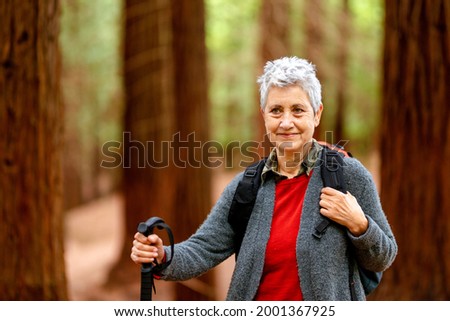 old woman with gray hair and backpack, performs exercise walking through a forest. Retirement and healthy life.
