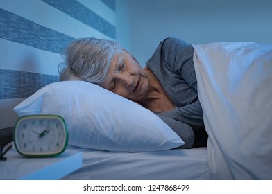 Old Woman In Grey Hair Sleeping Peacefully At Night Time In Bed. Senior Woman Lying On Side And Sleeping At Home. Mature Woman Feeling Relaxed At Home While Sleeping At Night.