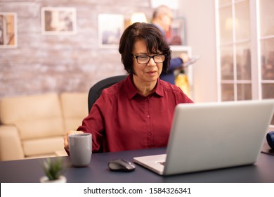 Old Woman In Her 60s Using A Modern Laptop In Her Cozy House Late In The Evening