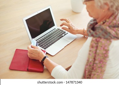 Old Woman Holding A Credit Card In Front Of Laptop With Blank Screen