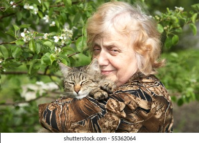 The old woman holds on hands cat against a blossoming tree