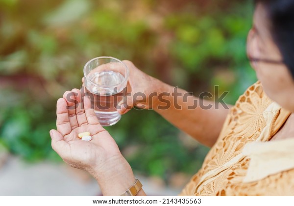 The old woman holds a pill in her\
hand with a glass of water to eat. Health care\
concept.