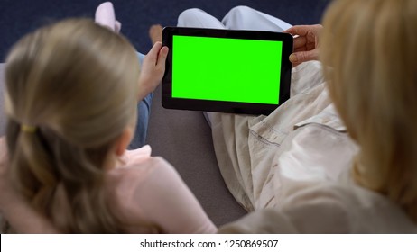 Old woman and little girl hands holding tablet with green screen, watching video
