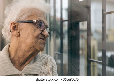 Old Woman Looking Out The Window. Concept About Aging And Loneliness