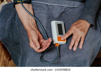 Old Woman Measures Blood Pressure And Pulse Using An Electronic Device. View From Above.