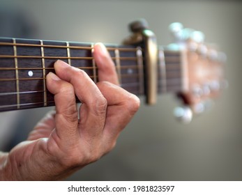 Old woman musician hand holds the neck of classic wooden guitar play Bm chord. Senior female guitarist put fingers on fingerboard playing B Minor chord song. String musical instrument background. 