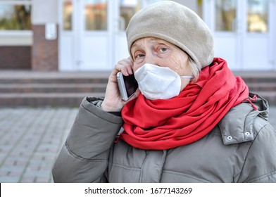 An Old Woman Near The Hospital Door In A Protective Mask On Her Face Is Talking On Her Cell Phone. Medical Help Older People. COVID-2019, Coronavirus. Senior Health.