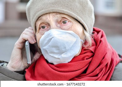 An Old Woman Near The Hospital Door In A Protective Mask On Her Face Is Talking On Her Cell Phone. Medical Help Older People. COVID-2019, Coronavirus. Senior Health.