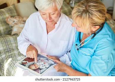 Old Woman And Nurse Look At A Photo Album Together