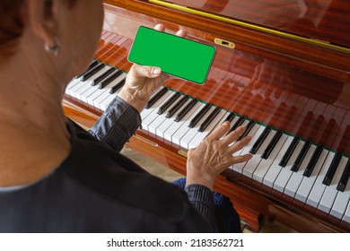 old woman plays the piano, looks into the phone notes. Chroma key on smartphone