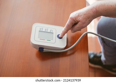 old woman presses the start button of a blood pressure monitor with her finger - Shutterstock ID 2124137939