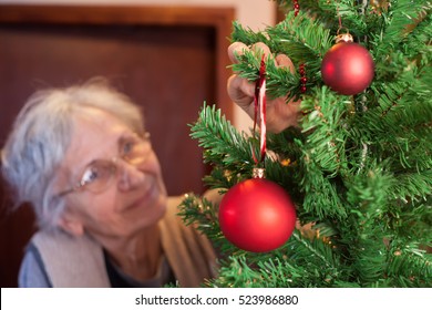 Old Woman Putting Ornaments On Christmas Tree