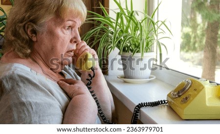 Old woman receives phone call from a scammer. Frightened grandmother talking on an old disc phone