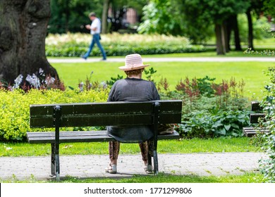 An Old Woman Rests In A Park Bench On A Sunny Summer Day