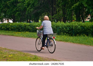 Old Woman Riding A Bicycle In The Park