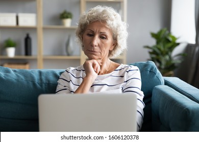 Old woman sit on couch looks at laptop screen feels confused, difficulties with modern gadgets, not understanding how it works, need assistance in learning to use devices and digital services concept - Powered by Shutterstock