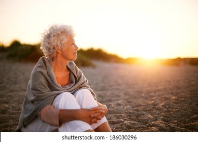 Old woman sitting on the beach looking away at copyspace. Senior female sitting outdoors - Powered by Shutterstock