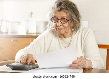 An old woman sitting at a table in the kitchen looking through receipts with a calculator