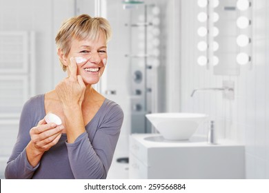 Old Woman With Skin Care Lotion Standing In A Bathroom (3D Rendering Of Background)