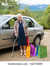 Old Woman Standing With Shopping Bags Near The Car