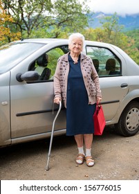 Old Woman Standing With Shopping Bags Near The Car