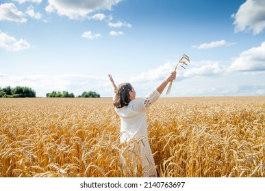 Old Woman  Stands With Her Back With Her Arms Spread Out To   Side In   Field With Golden Ears Of Cereal Crops 

