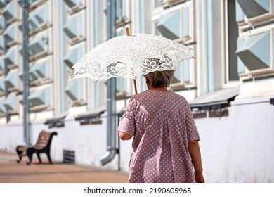 Old woman with sun umbrella walk on a street. Hot weather, life of elderly people in summer - Powered by Shutterstock