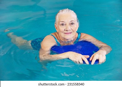 Old woman swimming in water with kickboard in a hotel pool