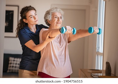 Old woman training with physiotherapist using dumbbells at home. Therapist assisting senior woman with exercises in nursing home. Elderly patient using dumbbells with outstretched arms. - Powered by Shutterstock