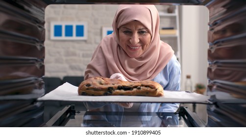 The Old Woman In A Turban Takes Out Delicious, Rich Grain And Olive Bread From The Oven. Shooting Through The Oven. 