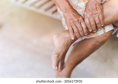 Old Woman Uses Her Hands To Massage Her Sore Ankle An Injury Due To Arthritis, Osteoporosis, Tendon Injury. Concept Of Sickness In The Elderly.