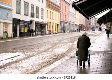 An Old Woman Walking Outdoors In The Winter With A Few Snow Crystals Visible In The Air. - Focus Is On The Woman With The Background Thrown Out Of Focus.