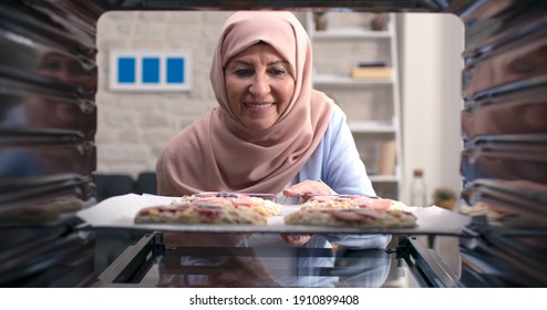 The Old Woman Wearing A Turban Puts Delicious, Tiny Pizzas From The Oven. Shooting From The Oven. 