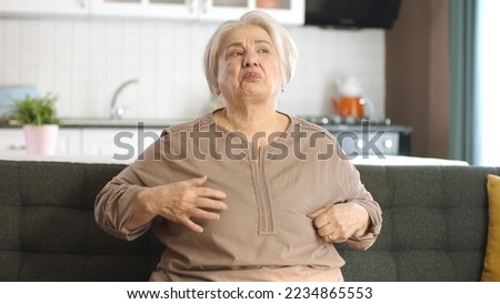 Old woman with white hair feels uncomfortable in clothes. Uncomfortable outfit concept. Restless old woman tugging at her unsuitable, badly fabricated outfit. Clothing allergy.