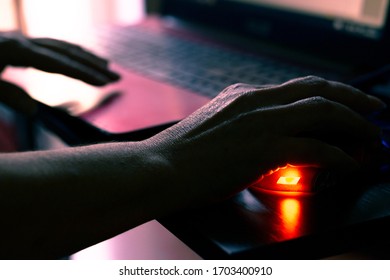 Old Woman Works On A Laptop. Work At The Computer In A Dark Room. A Wrinkled Hand Uses A Computer Mouse