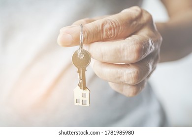 old woman's finger hold house key with blurred mini wooden house , close up