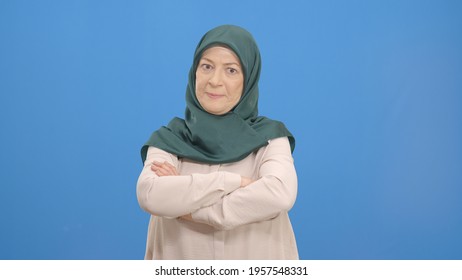 Old Women Wearing Headscarves Are Very Angry With What Happens. She Explains That She Was Angry With Her Arms Crossed On Her Chest. Portrait Of The Angry Old Lady. Indoor Studio Shot Isolated On Blue 