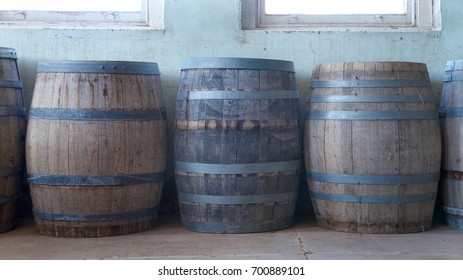 Old Wood Barrels Lining A Worn Weathered Wall In The Basement Of An Old Building. Used For Food Storage In Early American History