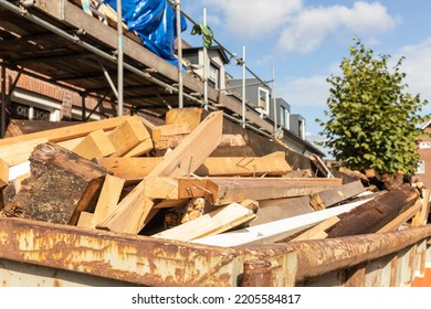 Old Wood Demolition Waste, From Destruction Or Renovation Of Buildings In A Container On A Work Site In A Street With A House. Wooden Beams To Be Recycled Into New Building Materials. Circular Economy