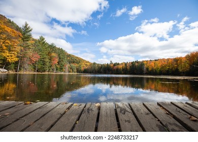 The old wood dock with the autumn forest landscape in the background reflected on the still waters of the lake 