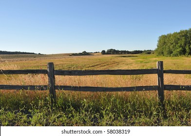 An old wood fence with a green country field behind it.