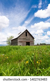 Old wooden barn in the field with blue skies and clouds above.